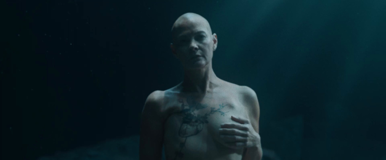 a man with a tattoo on his chest standing in the dark