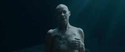 a man with a tattoo on his chest standing in the dark