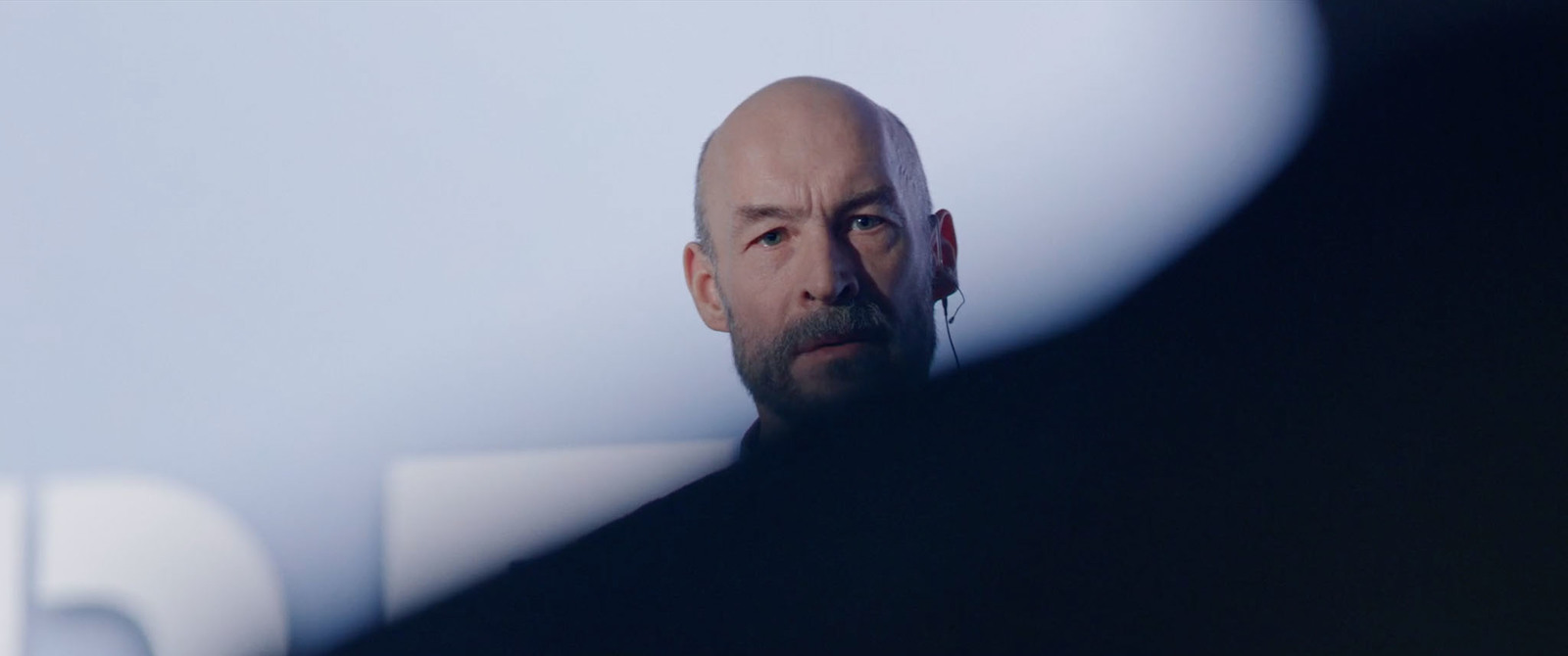 a bald man with a goatee stares into the distance