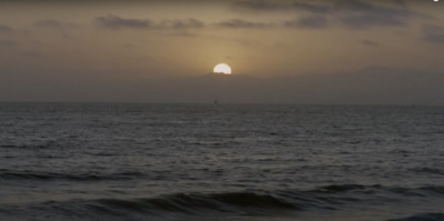 the sun is setting over the ocean on a cloudy day