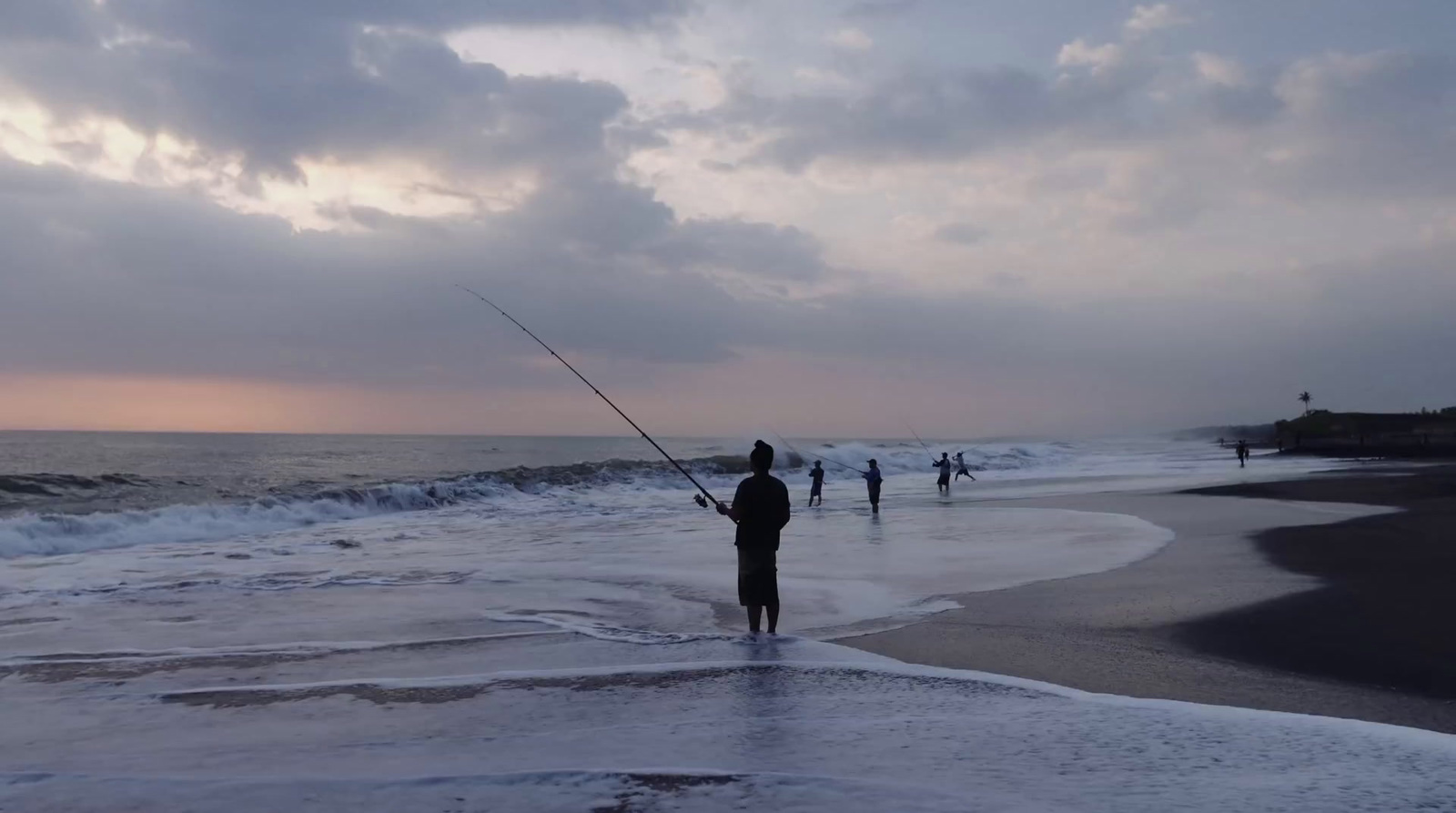 a man standing on top of a beach holding a fishing pole