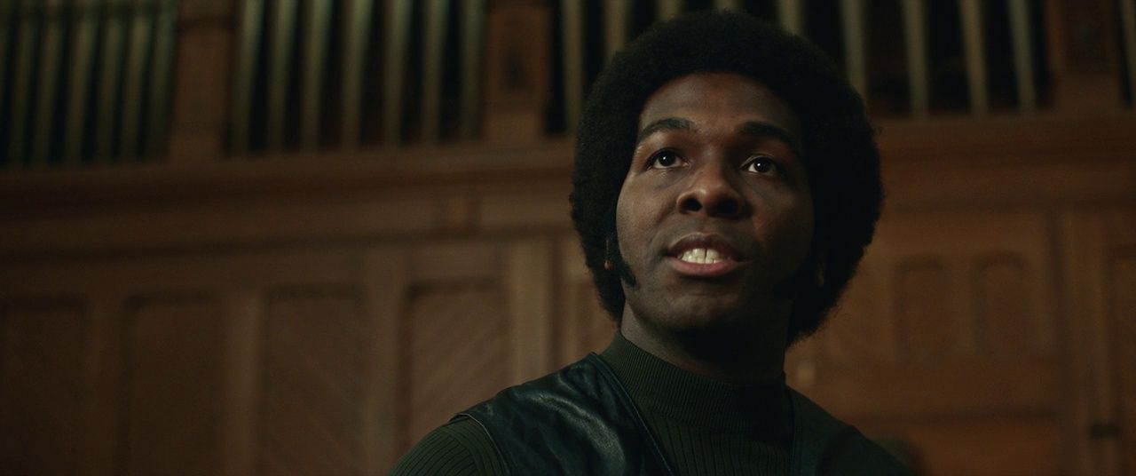 a man in a green shirt standing in front of a pipe organ