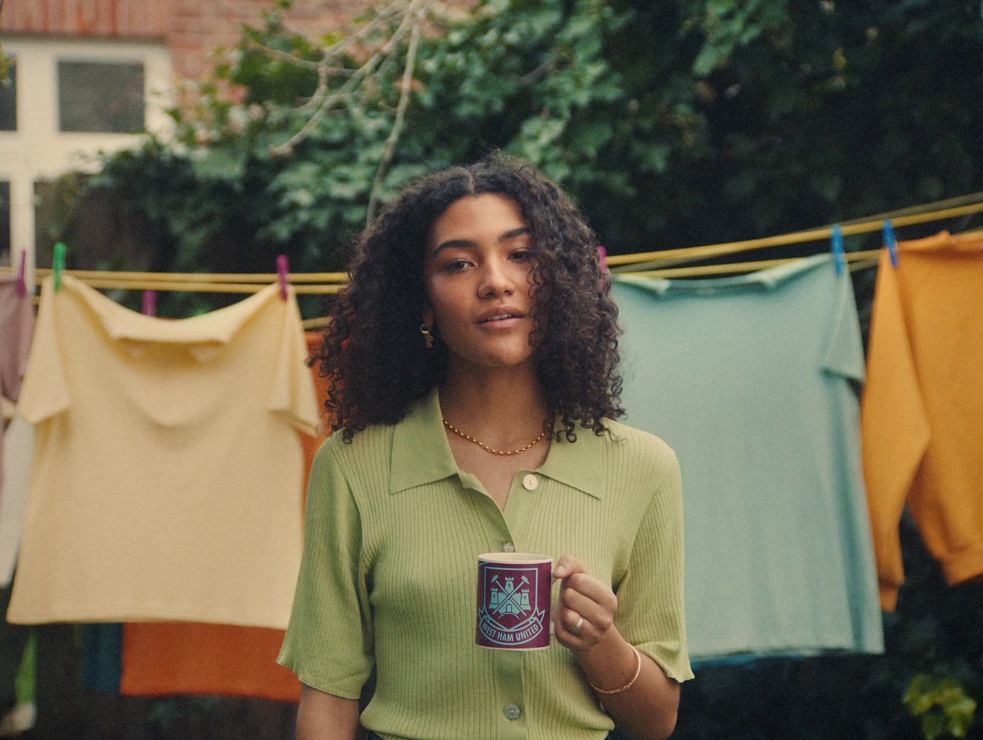 a woman holding a cup of coffee in front of clothes hanging on a line