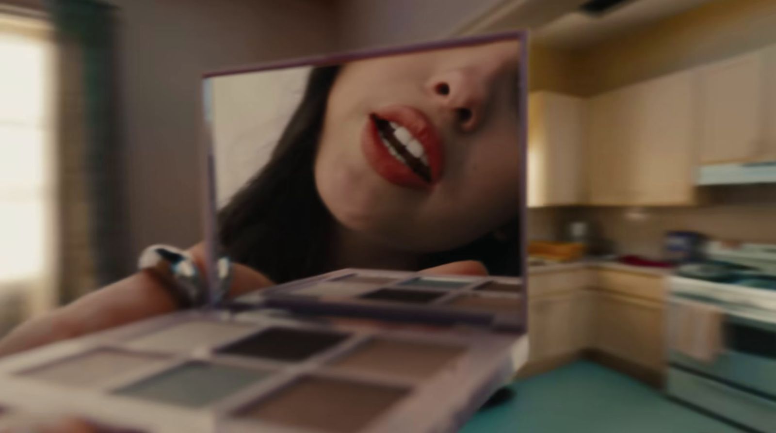 a woman holding a makeup palette in a kitchen