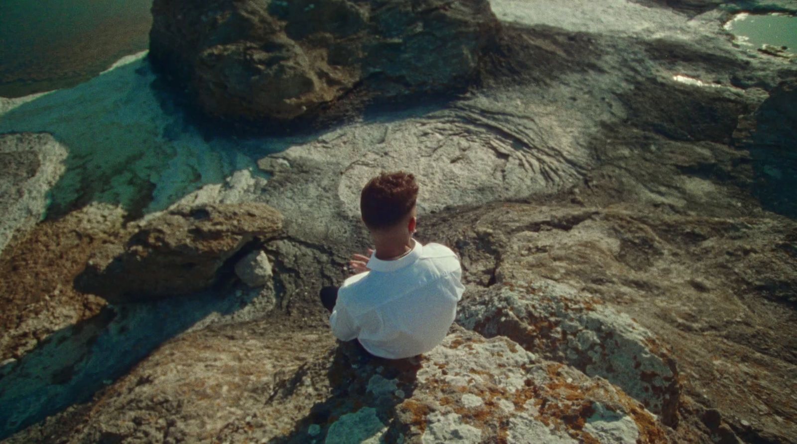 a man sitting on top of a rock next to a body of water