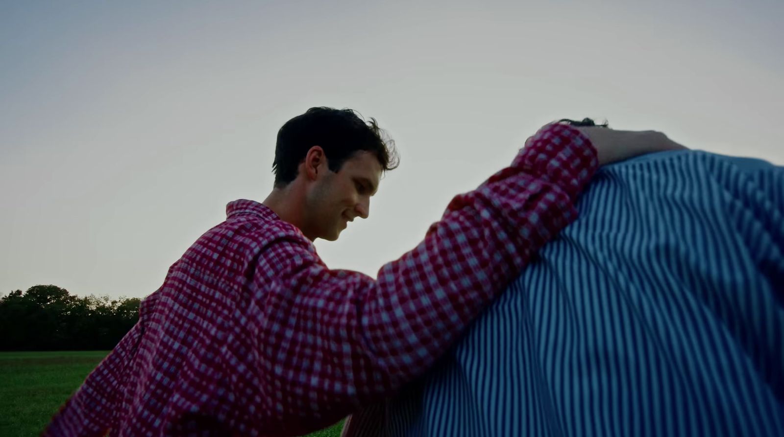 a man in a red and white checkered shirt leaning against a blue and white