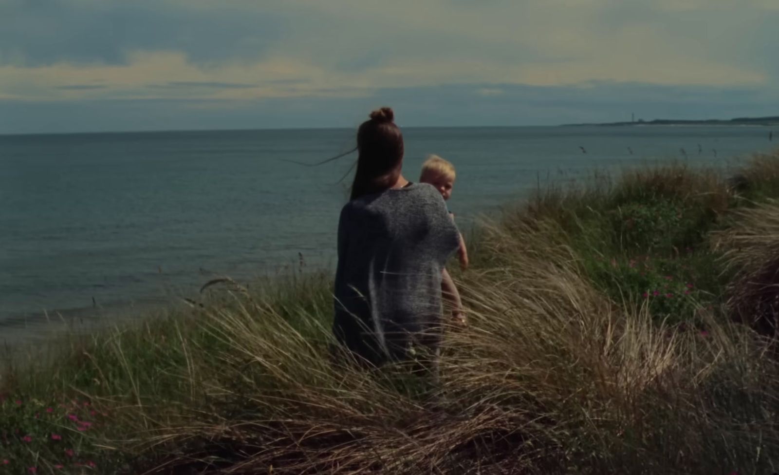 a woman and a child standing on top of a grass covered hillside