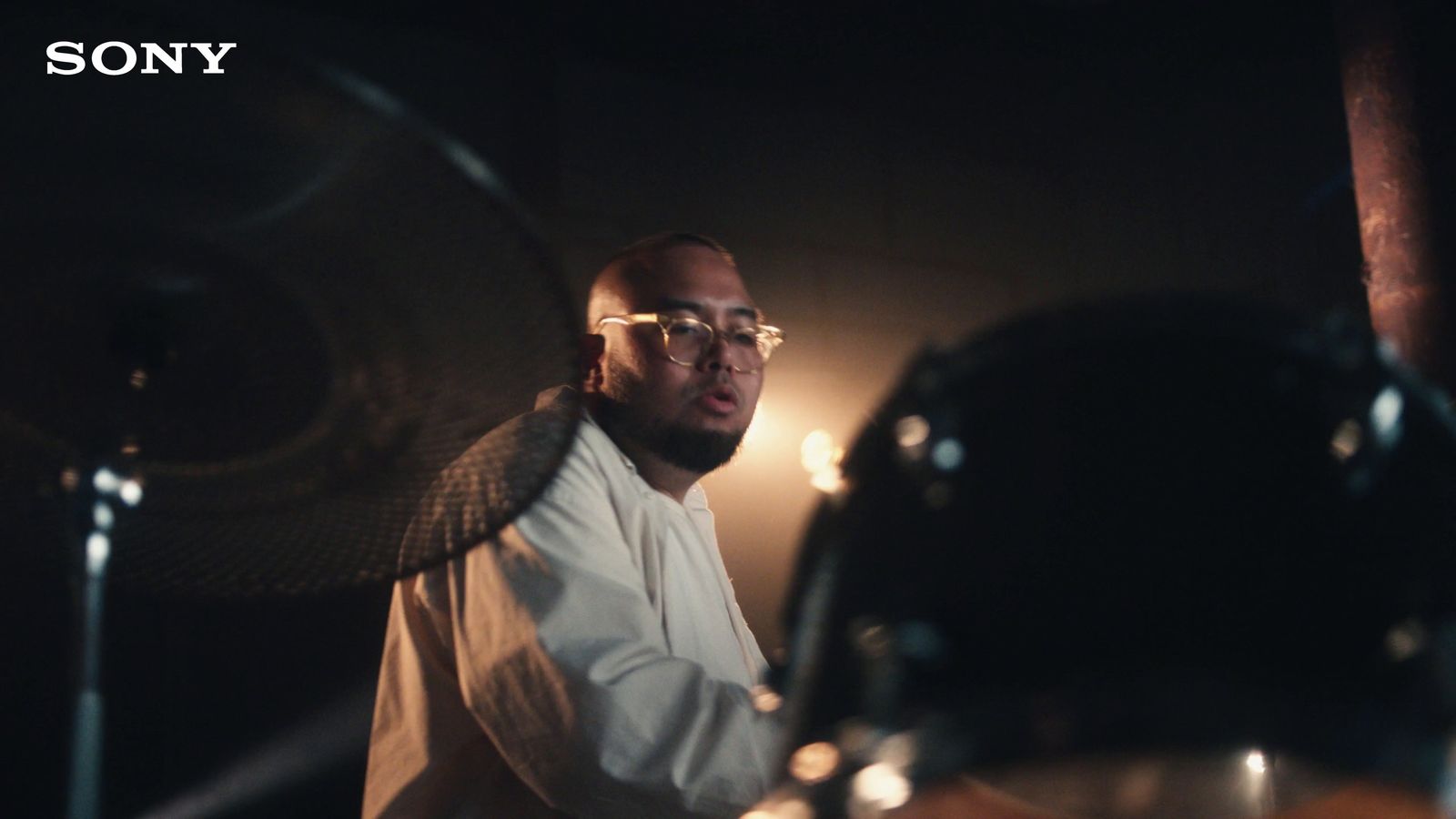 a man with glasses playing drums in a dark room