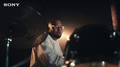 a man with glasses playing drums in a dark room