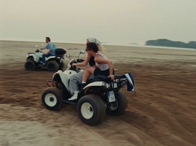 two people riding four wheelers on a sandy beach