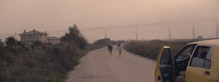 two people walking down a dirt road next to a yellow truck