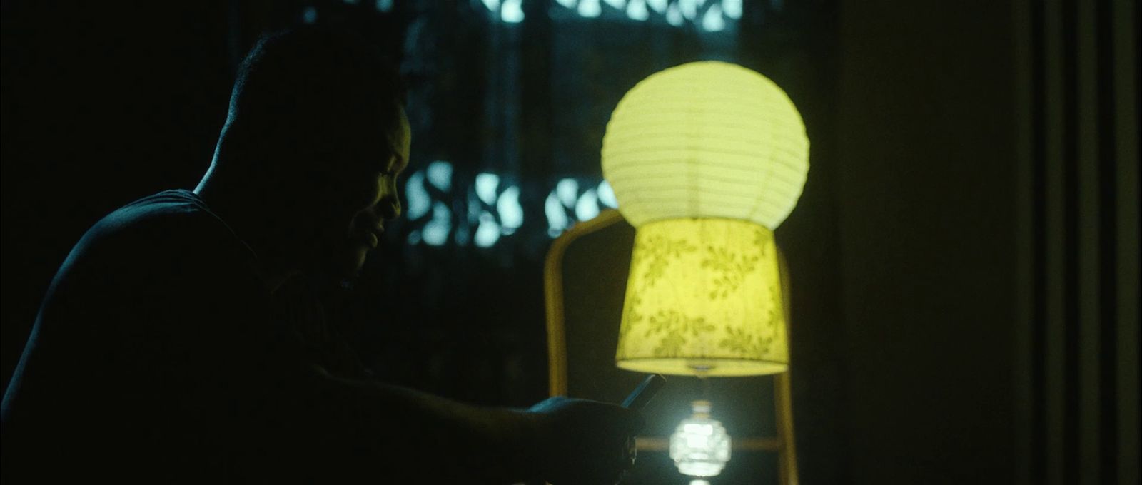 a man sitting in a dark room next to a lamp