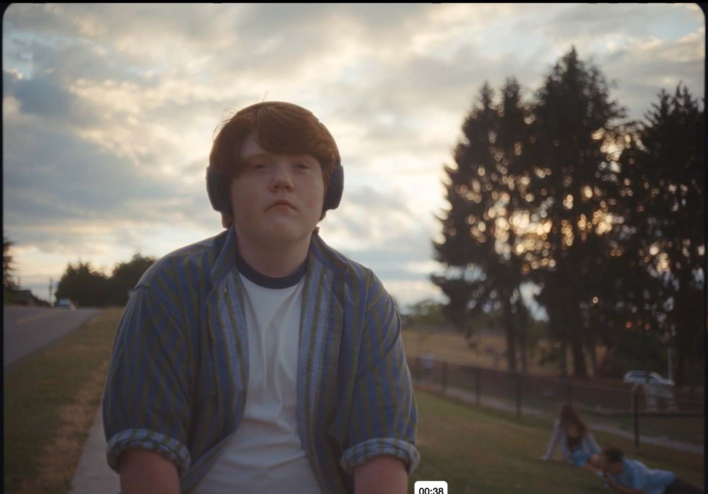 a young man wearing headphones standing in a park