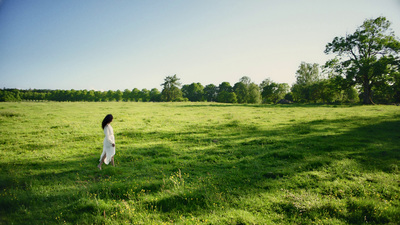 a woman in a white dress walking across a lush green field