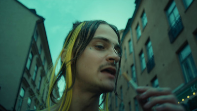 a man with long hair standing in front of a building