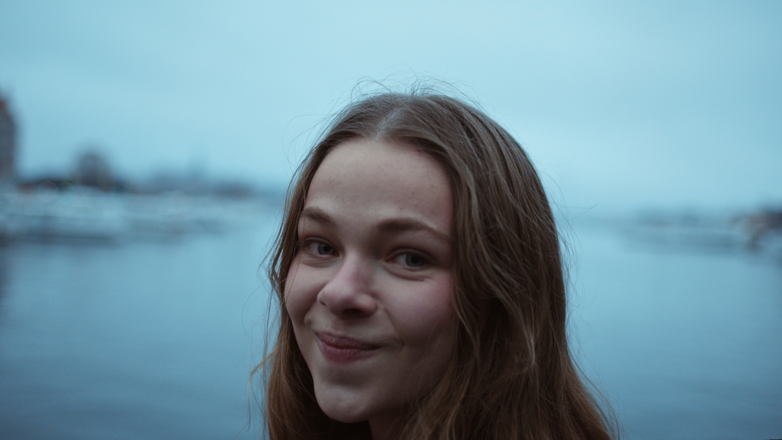 a woman with long hair standing in front of a body of water