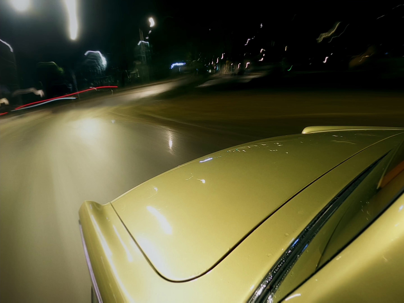 a yellow car driving down a street at night