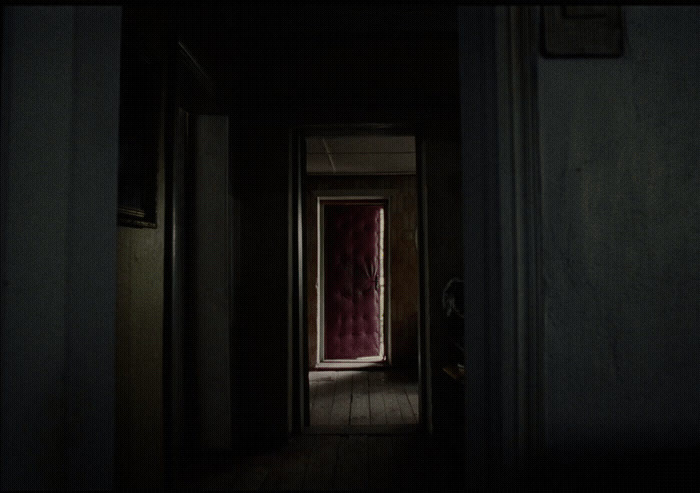 a dark hallway with a red door and a red curtain