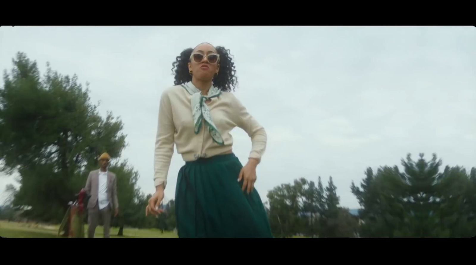 a woman standing in a field with a man behind her