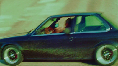 a blue car driving down a sandy road