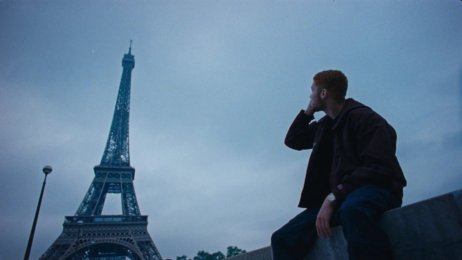 a man sitting on a wall in front of the eiffel tower