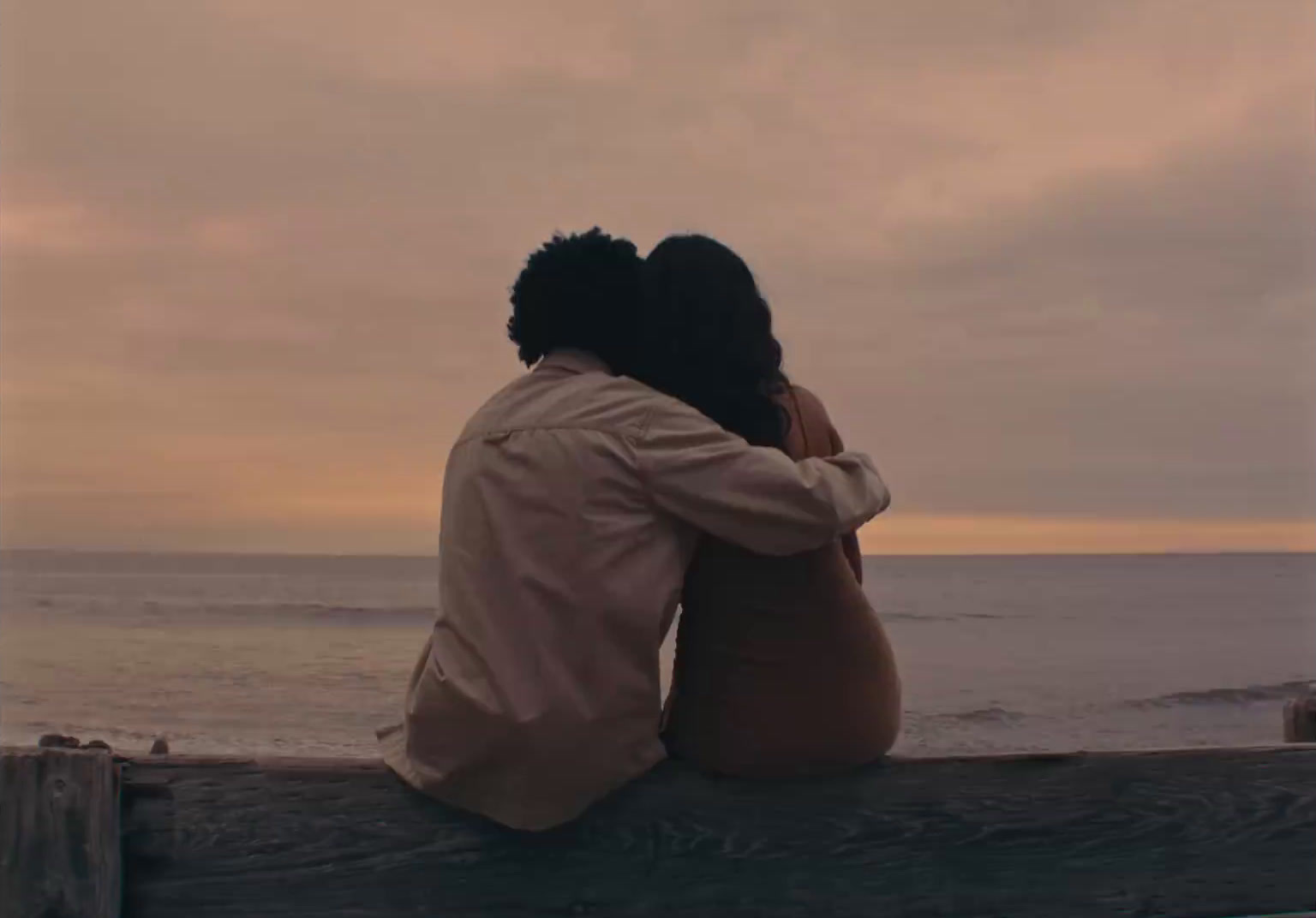 a man and a woman sitting on a bench looking out at the ocean