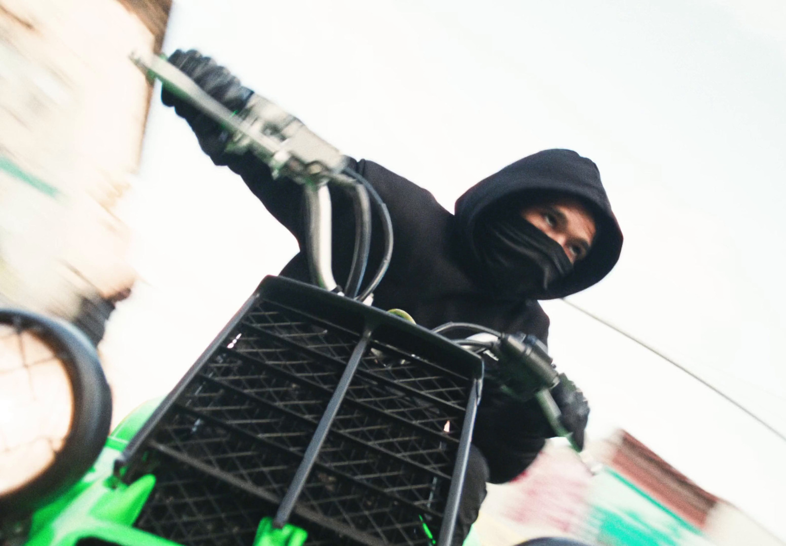 a man in a black hood is riding a green vehicle