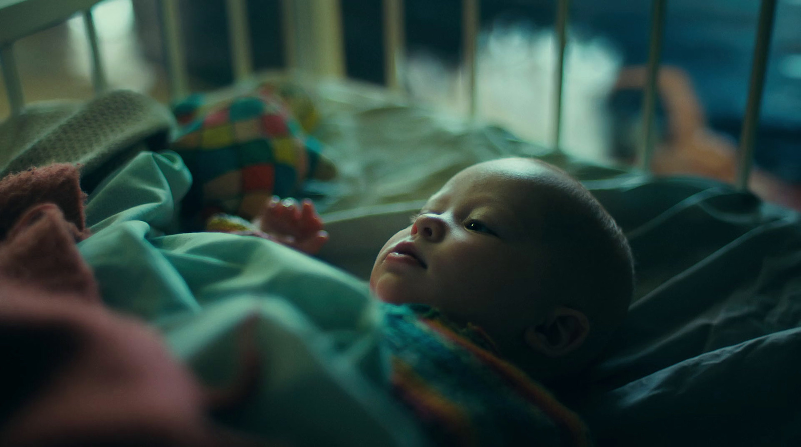 a baby laying in a crib with a blanket