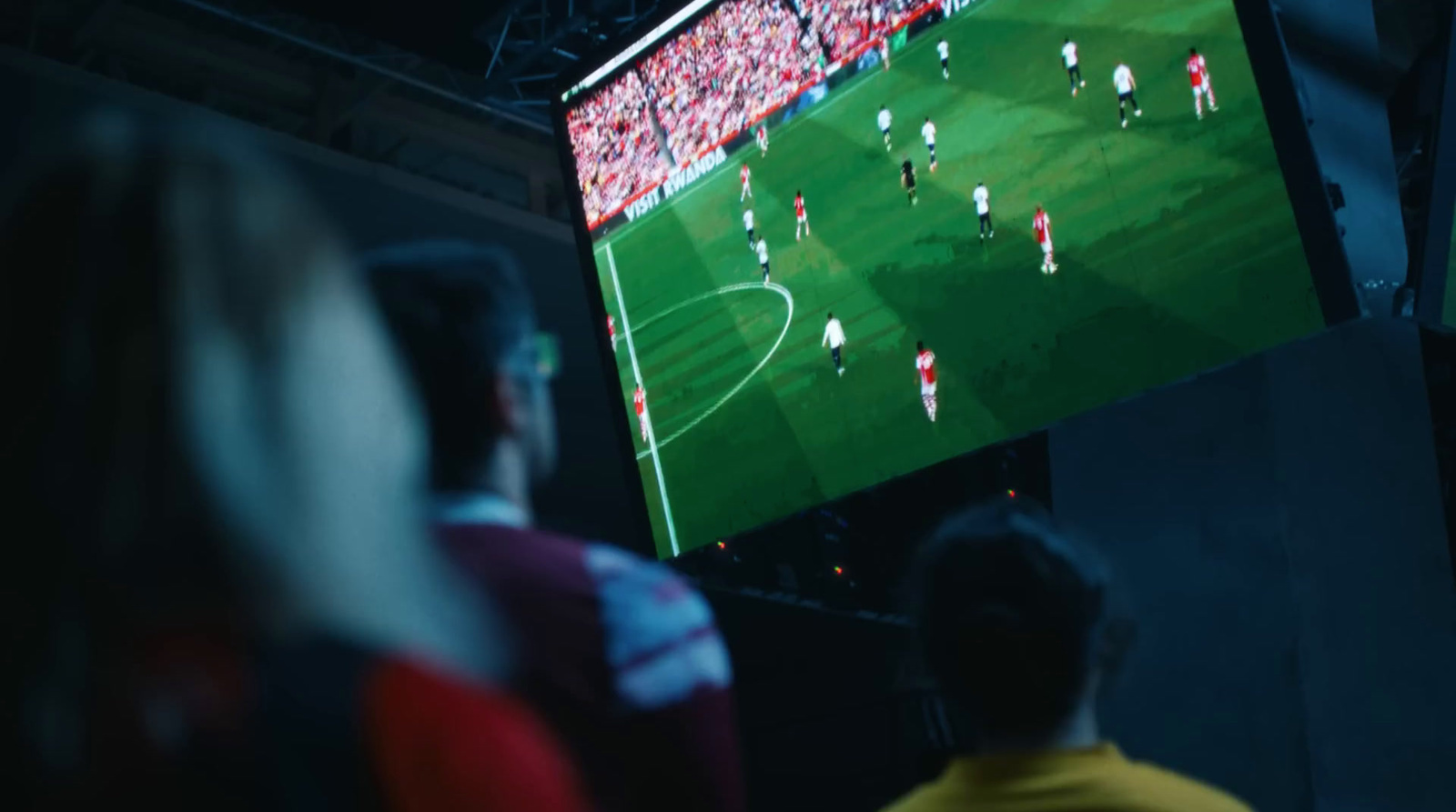 a group of people watching a soccer game on a big screen