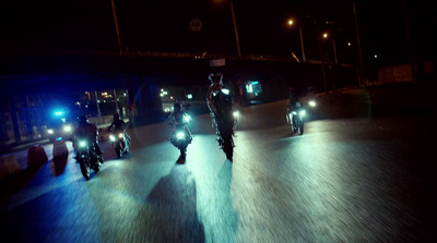 a group of people riding motorcycles down a street at night