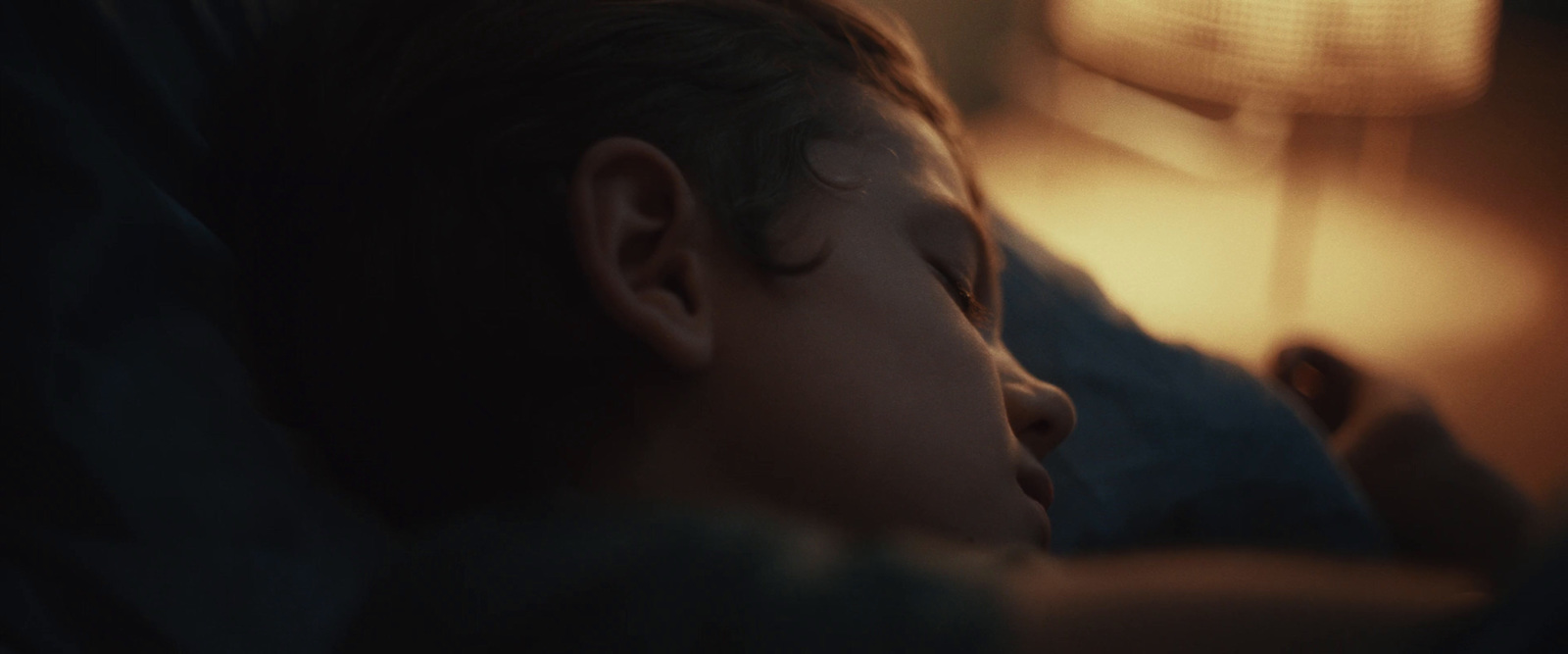 a young boy sleeping on a bed next to a lamp