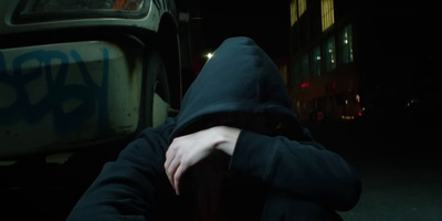 a person in a hoodie leaning against a car