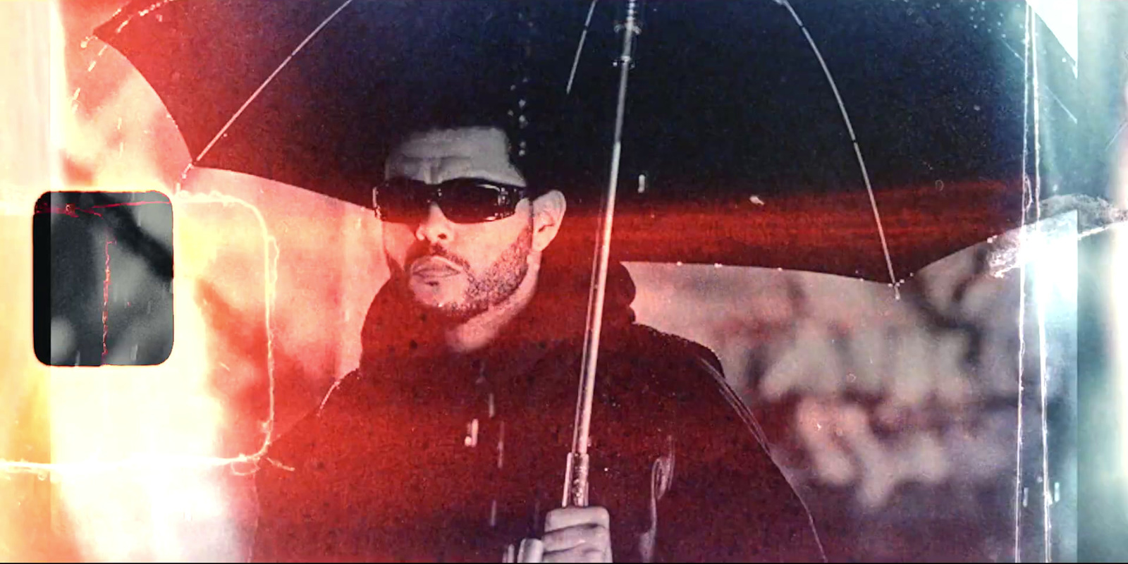 a man with sunglasses holding an umbrella in the rain