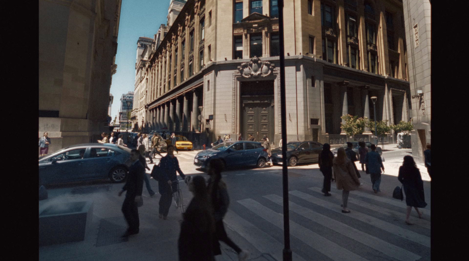 a group of people walking across a street next to tall buildings