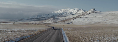 a truck driving down a road in front of a snow covered mountain