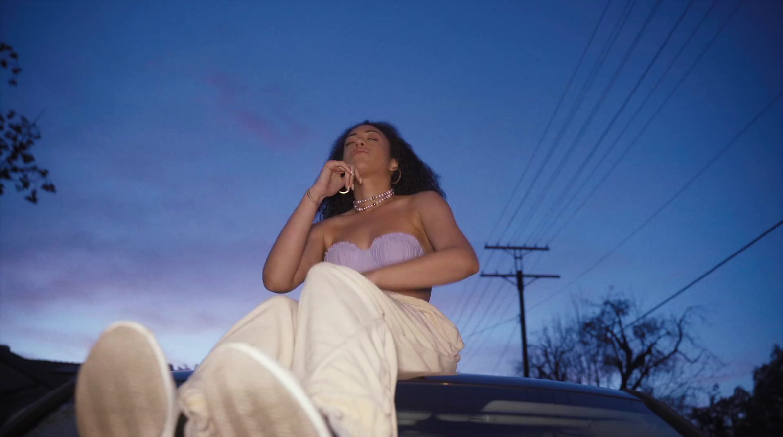 a woman sitting on top of a car talking on a cell phone