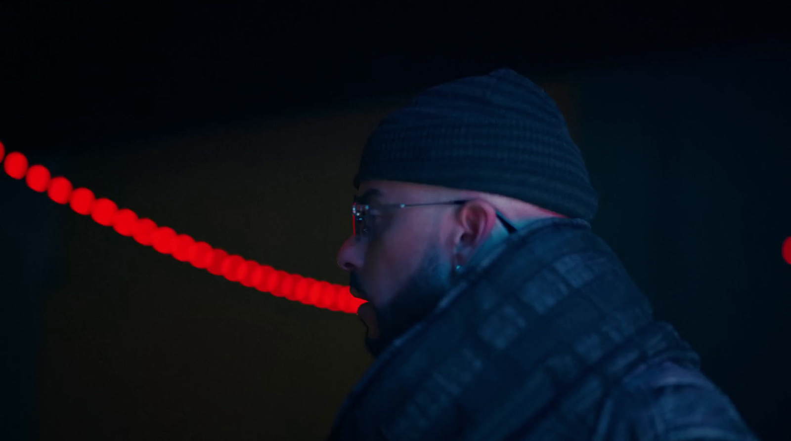 a man wearing a beanie and glasses in a dark room