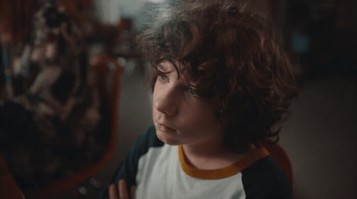 a young boy with curly hair looking at a mirror