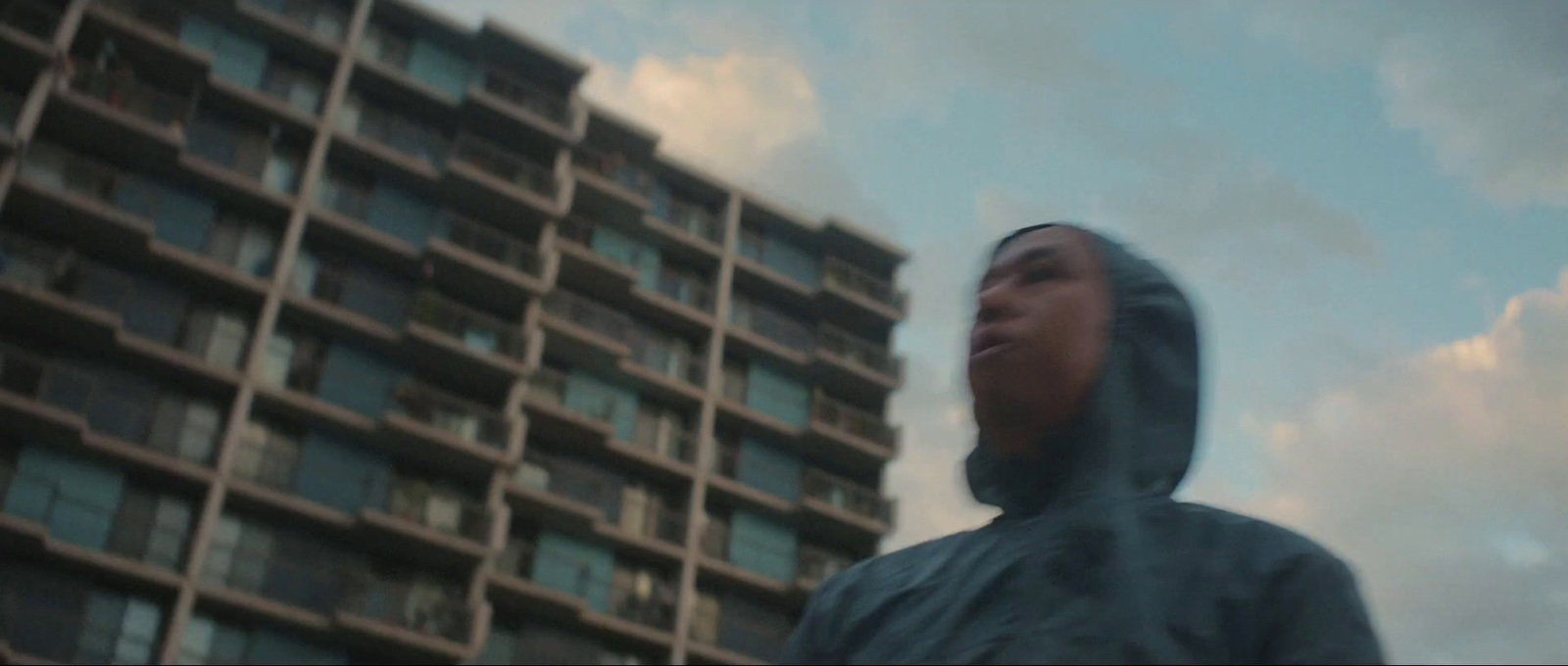 a man in a hooded jacket standing in front of a tall building