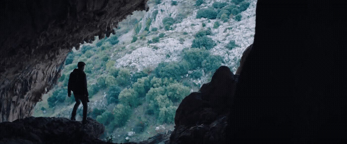 a man standing in a cave looking out at the water