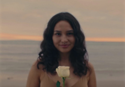 a woman holding a white rose in front of the ocean