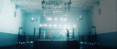 two people standing in a boxing ring surrounded by lights