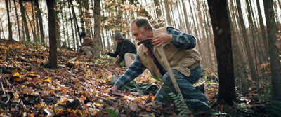 a group of people walking through a forest filled with leaves