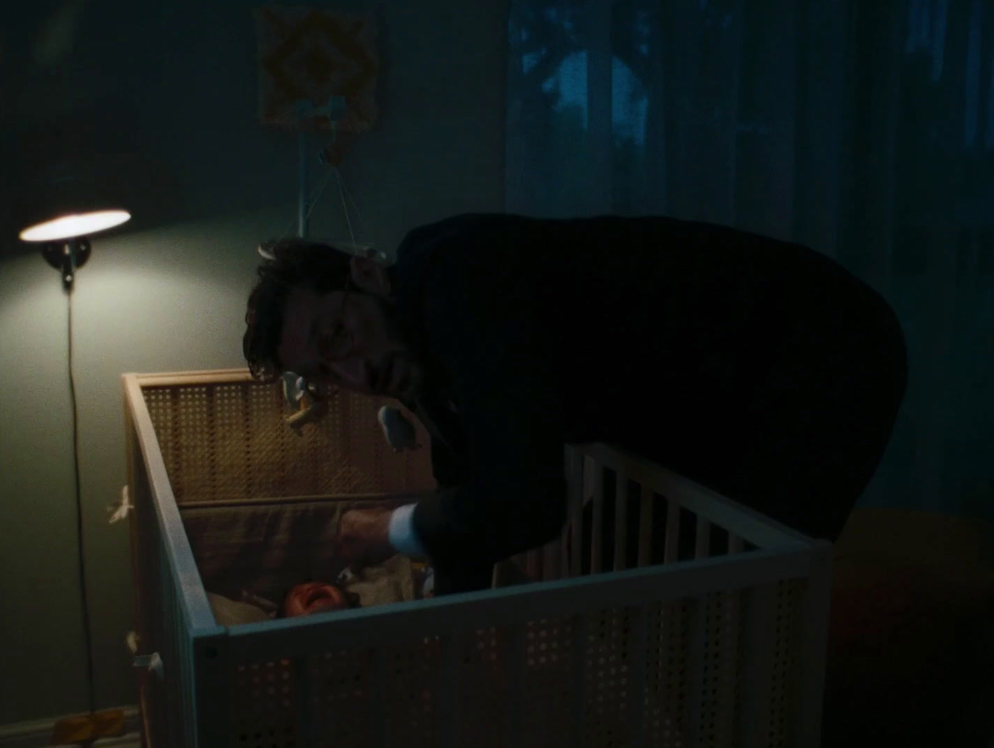 a man leaning over a crib in a dark room