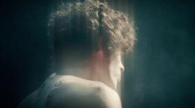 a man with curly hair standing in front of a window