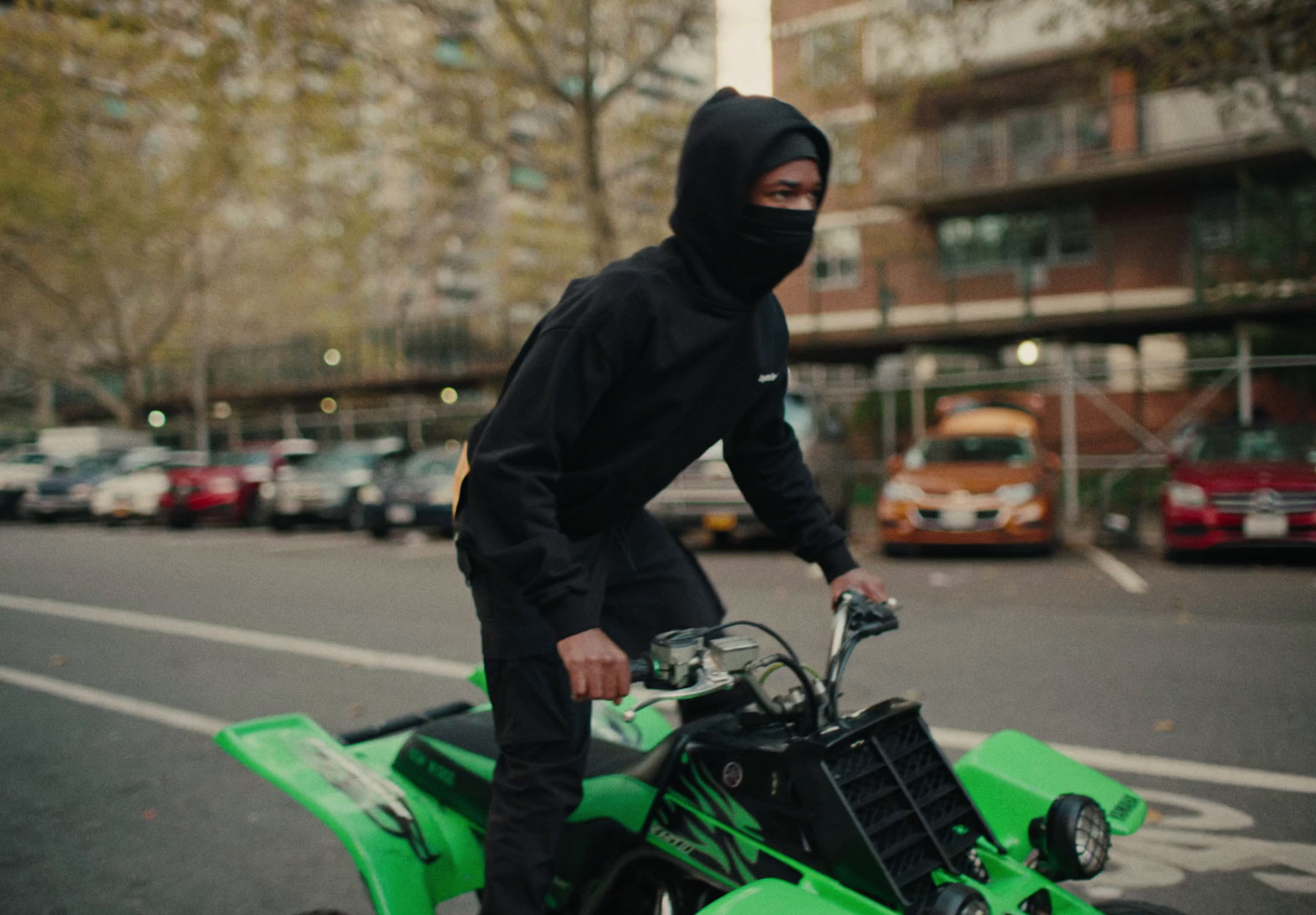 a man in a black hoodie riding a green atv