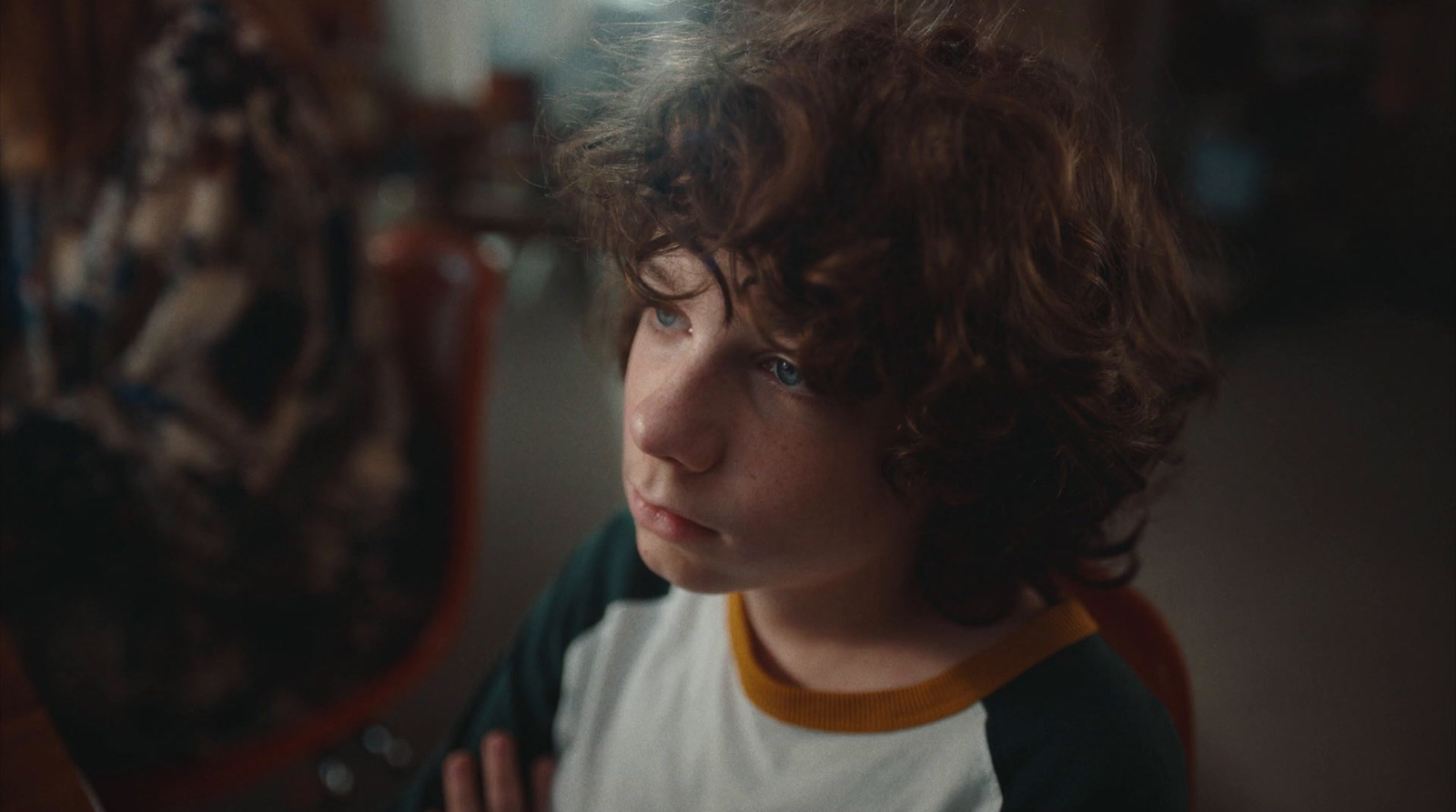 a young boy with curly hair sitting in a chair