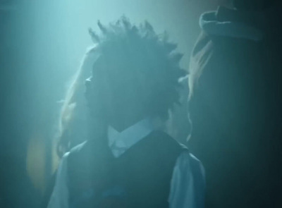 a man with dreadlocks standing in a dark room