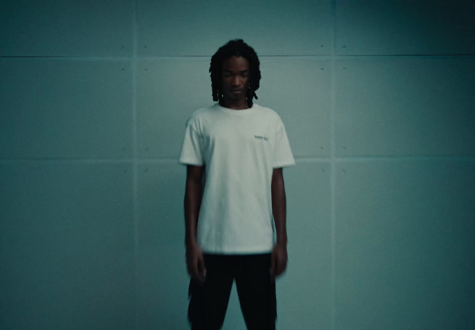 a man standing in front of a wall wearing a white t - shirt