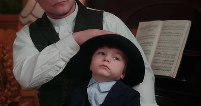 a young boy wearing a suit and tie standing next to a man in a hat